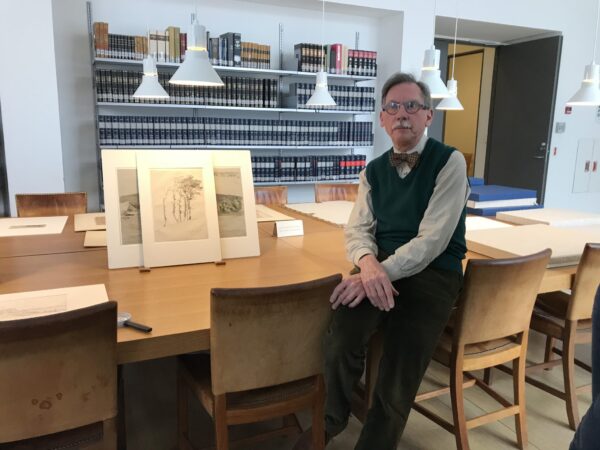 Man sits next to works on paper in the object study room