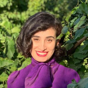a woman looking at the camera and smiling next to a green bush