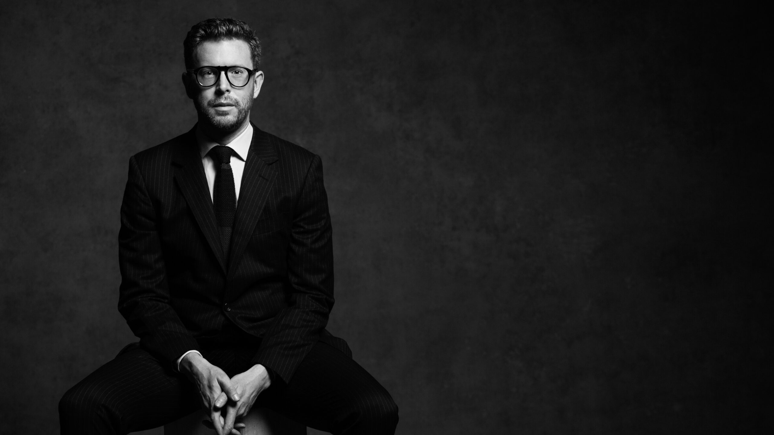 back and white portrait of a man wearing glasses standing and looking into the camera