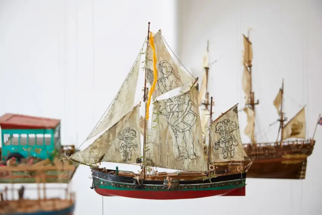 colourful miniature hand made boats suspended in a gallery by artist Hew Locke