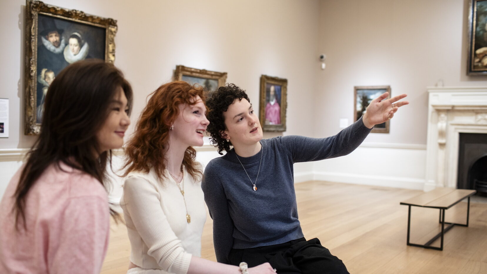 Three female students sat on a bench in The Courtauld Gallery Blavatnik Fine Rooms, discussing an artwork out of shot.